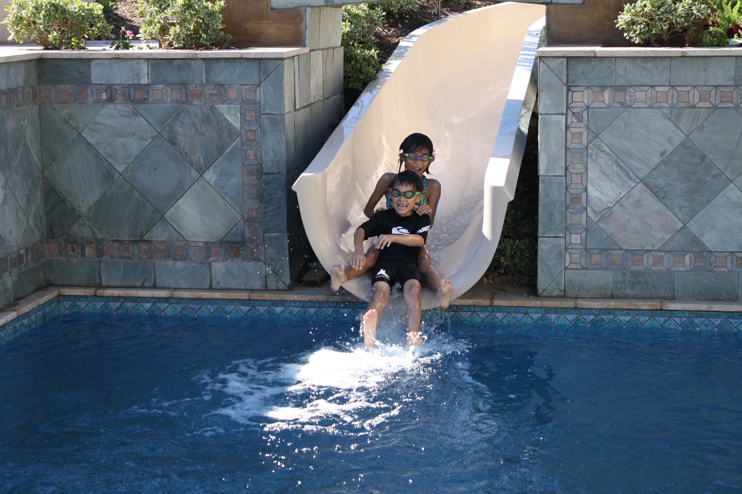Two young boys enjoy sliding into the grandparents backyard pool