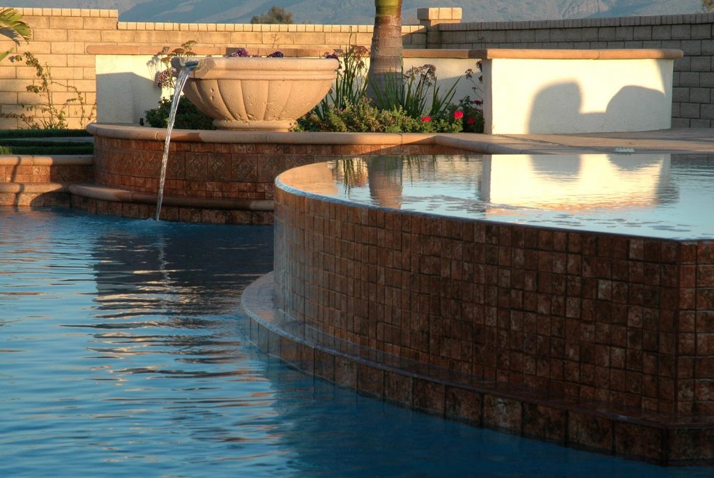A perimeter overflow spa by a swimming pool and a water fountain feature